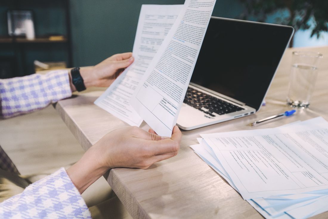 Person holding printed pages next to an open laptop on a desk, reviewing content across formats