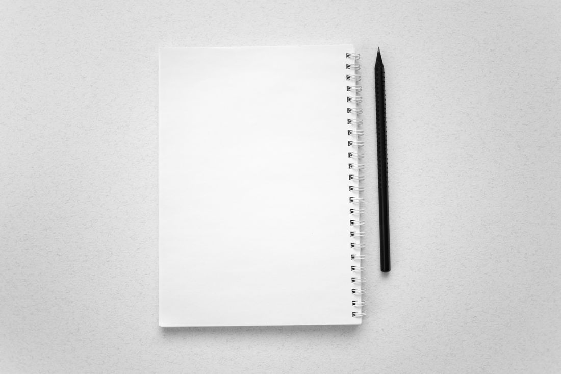 A blank spiral notebook and a pencil laid flat on a plain desk surface, viewed from directly above.