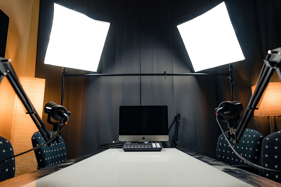 An empty podcast recording setup with studio lighting, microphones, and a monitor, ready for a session