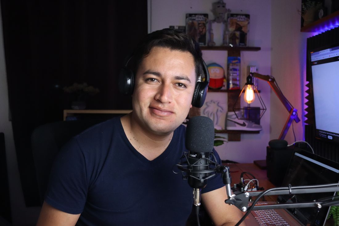 A podcast host wearing headphones, seated in front of a microphone in a home studio