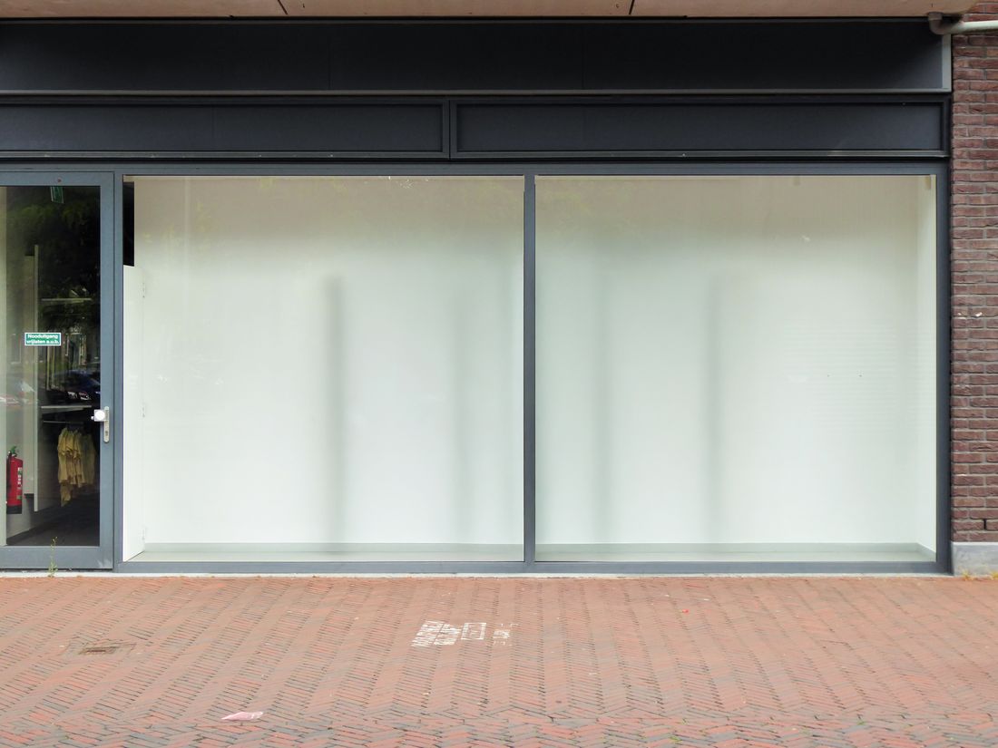A dark-framed storefront with blank, frosted display windows sits empty on a city sidewalk before build-out.