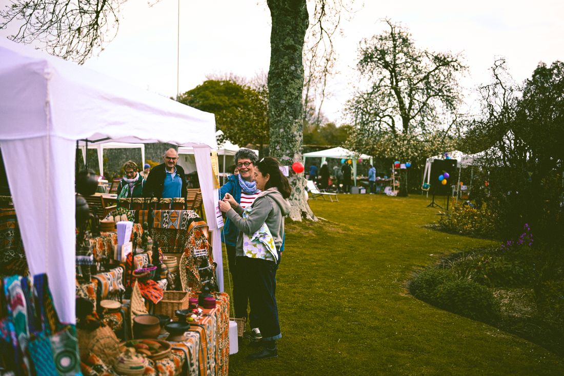 Visitors browse a row of white pop-up tents set up outdoors in a park for a temporary market.