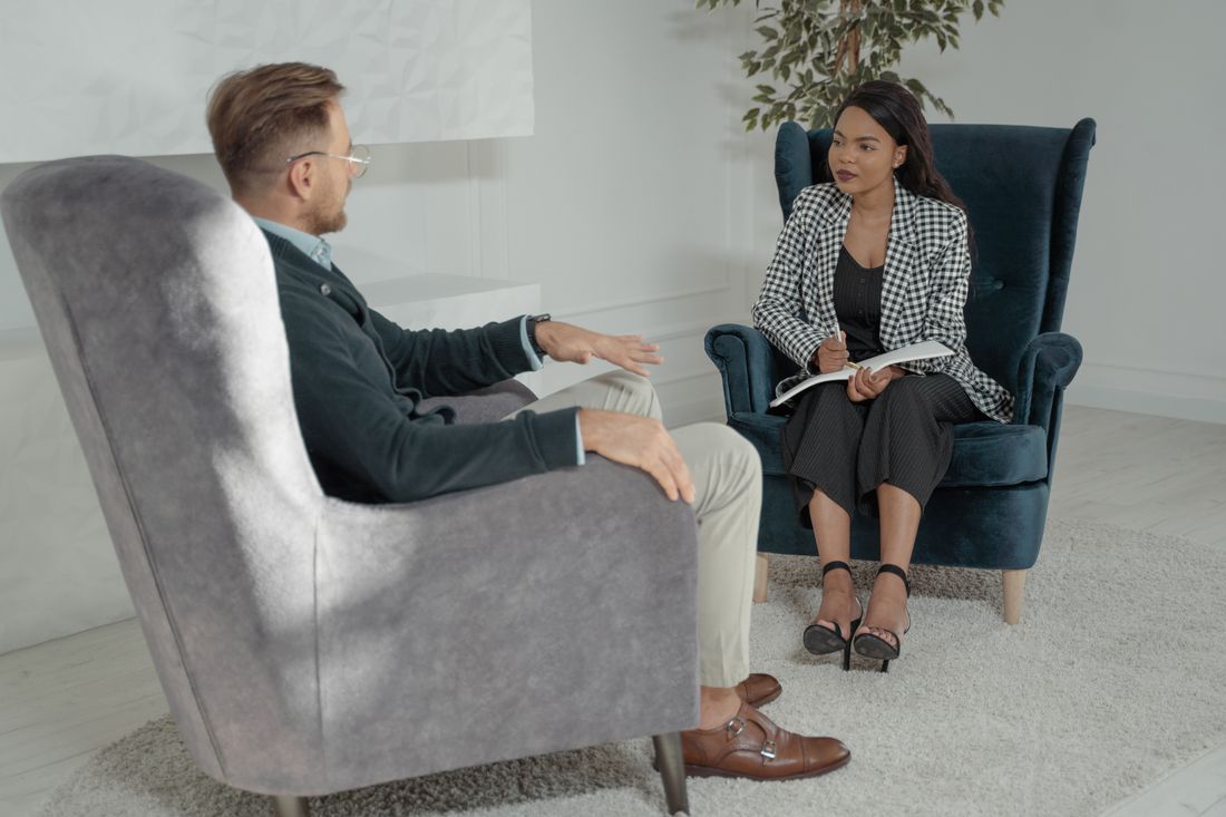 A man and a woman sit facing each other for a one-on-one interview in a modern office setting.