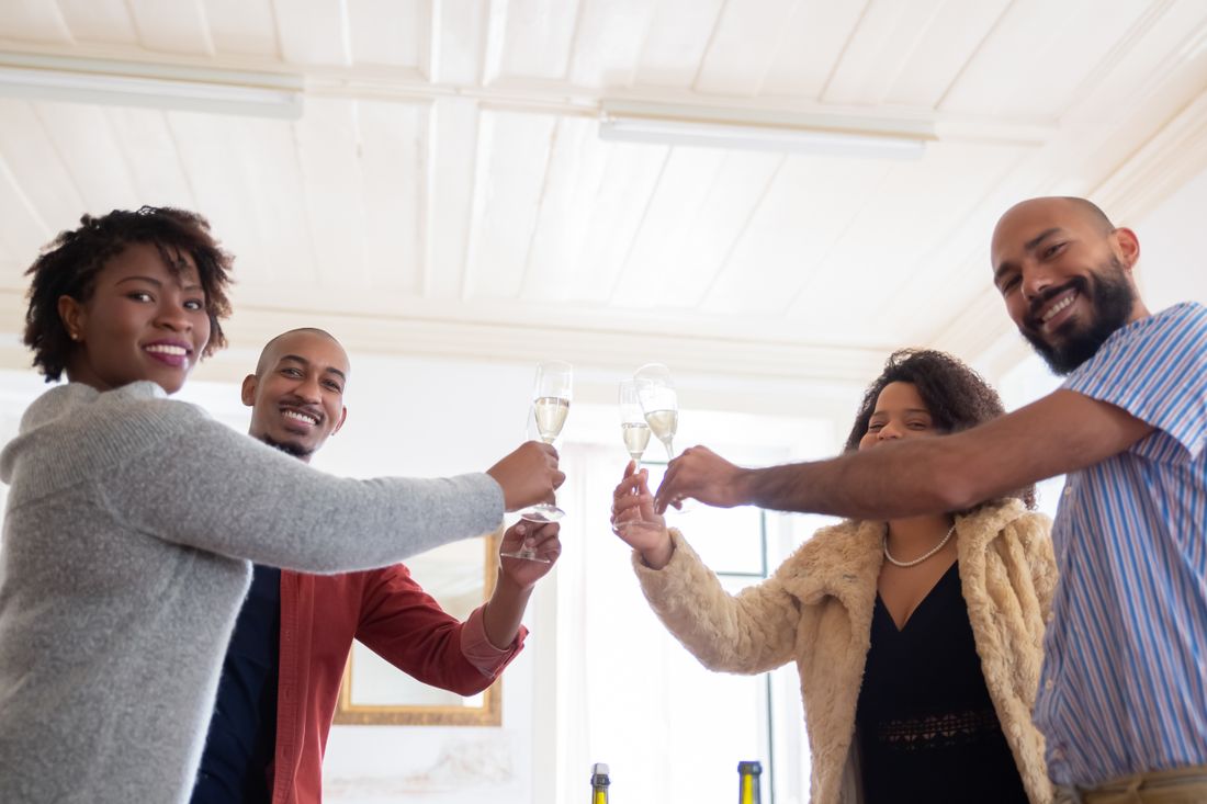 Four colleagues in a bright room reaching in to clink champagne flutes together, seen from below.