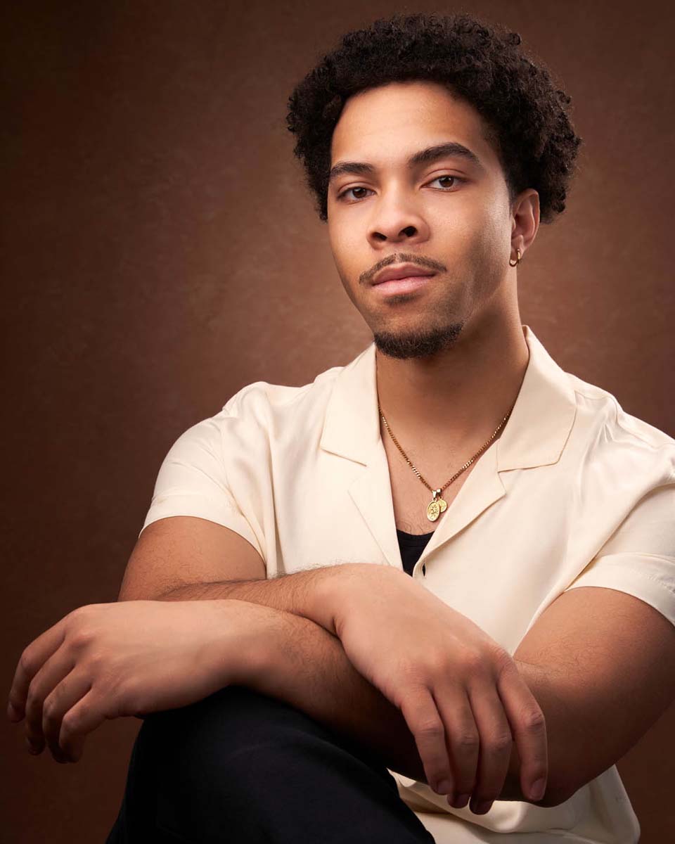Man in cream shirt poses calmly for professional headshot against warm backdrop.