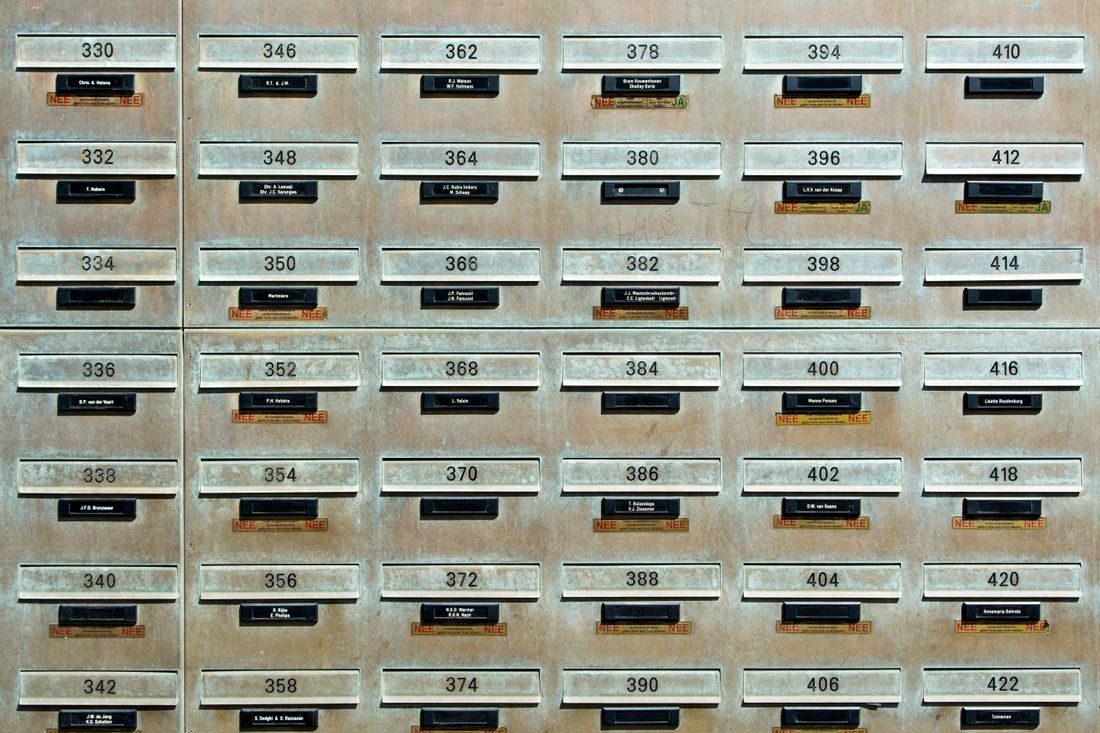 A wall grid of numbered metal mailbox doors, representing traditional paid mailboxes