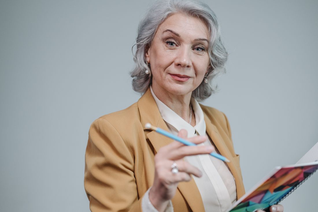 Studio portrait of a woman in a blazer holding a notebook, illustrating the approachable, credible register academic headshots aim for