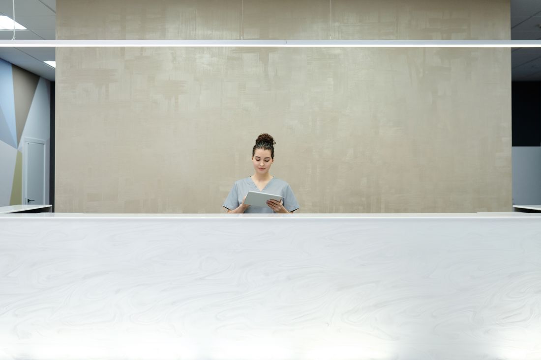 A receptionist at a front desk in a bright modern building lobby, using a tablet