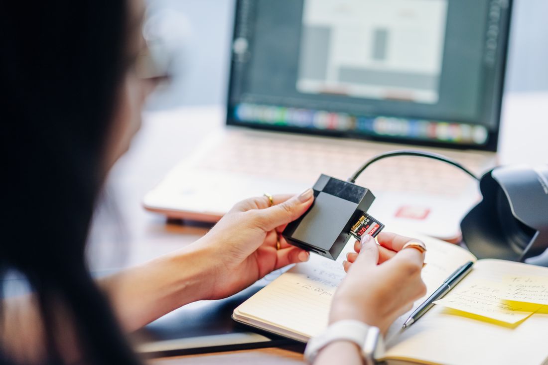 Person inserting an SD memory card into a card reader next to a laptop