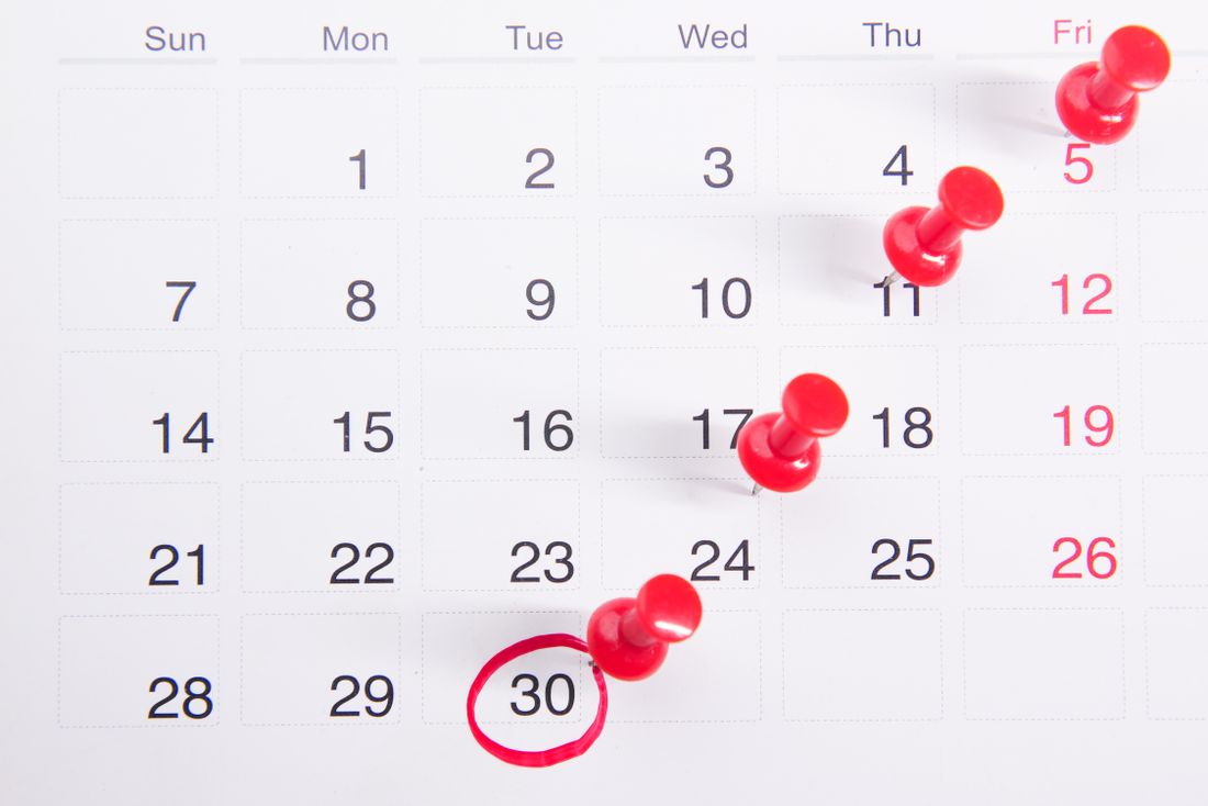 Close-up of a calendar with red push pins marking multiple important dates