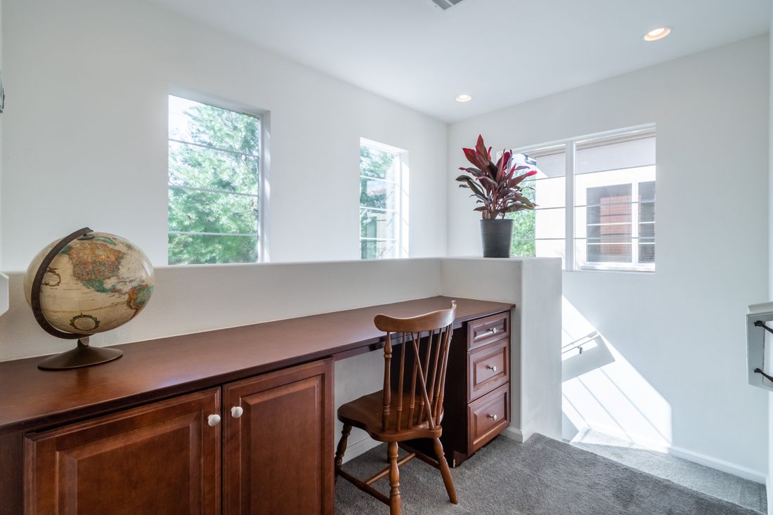 A tidy home workspace nook with a wooden desk, single wooden chair, small decorative globe, and windows letting in daylight, no people present.