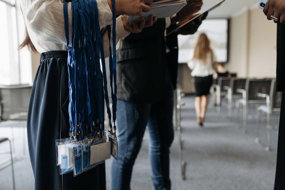 Rows of conference lanyards and name badges being organized ahead of an event, with chairs and a presentation screen in the background.