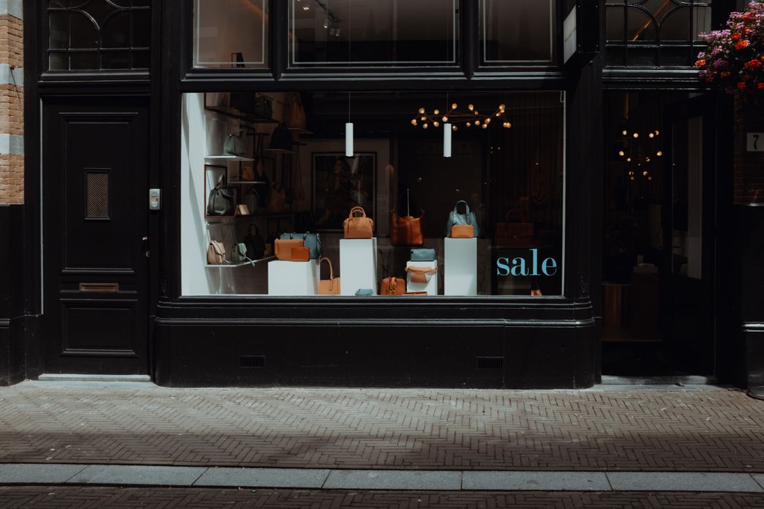 A dark shopfront with a lit window display seen from the sidewalk on a quiet street