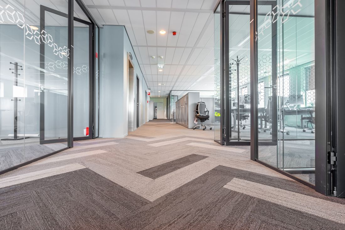A glass-walled office corridor leads past open conference rooms with desks and chairs visible on either side.