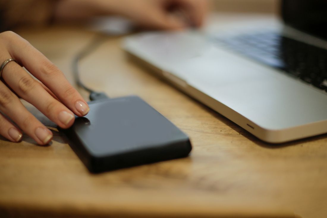 Close-up of a hand connecting an external hard drive to a laptop on a wooden desk for a backup transfer