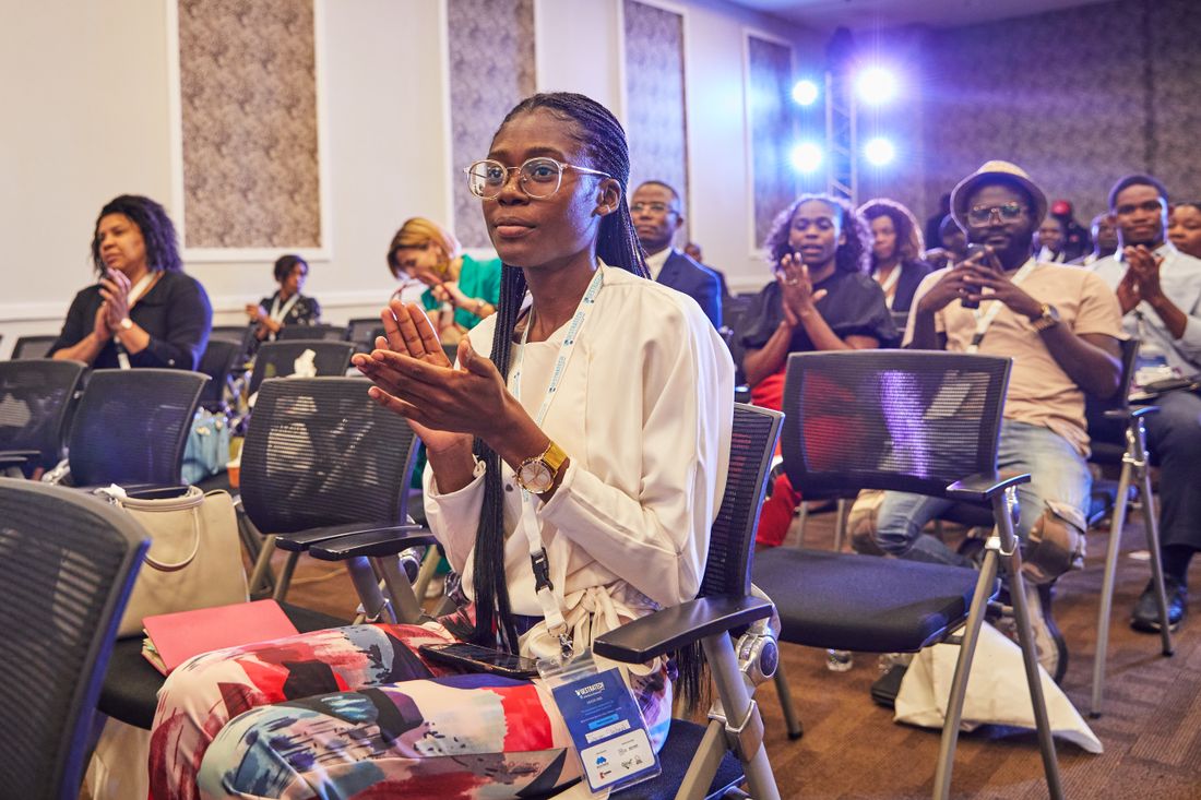 A woman claps enthusiastically while seated among other attendees at an indoor business conference.