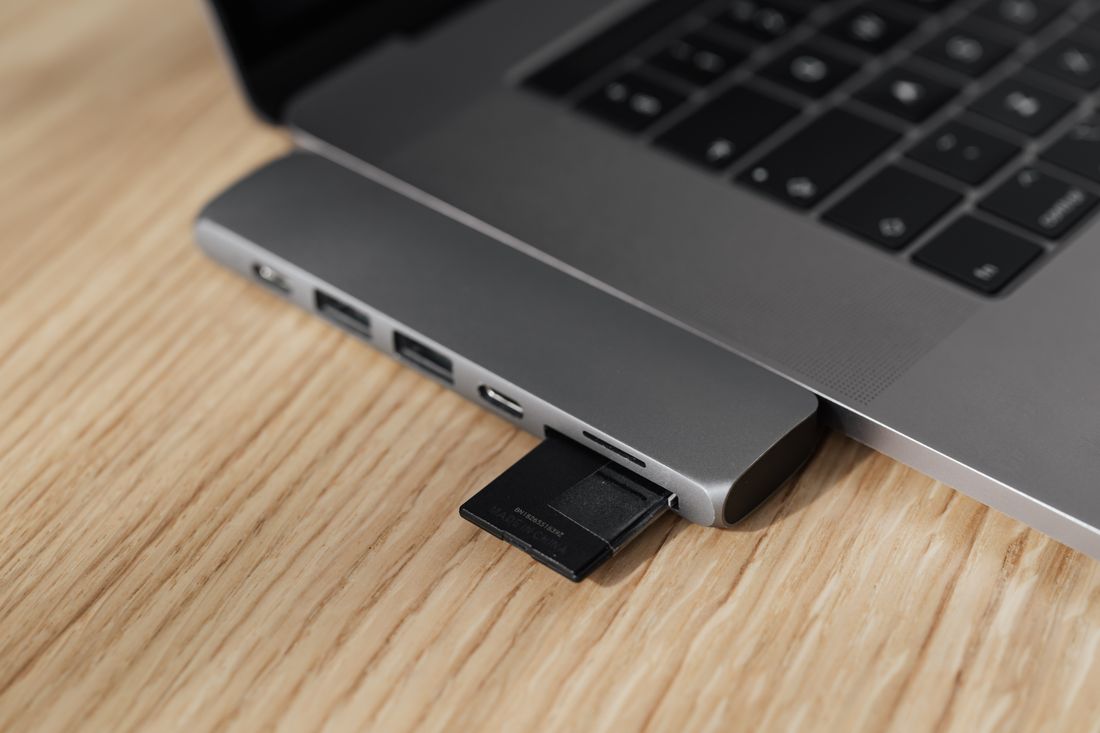 Memory card being inserted into a laptop's USB hub on a wooden desk for on-site photo transfer