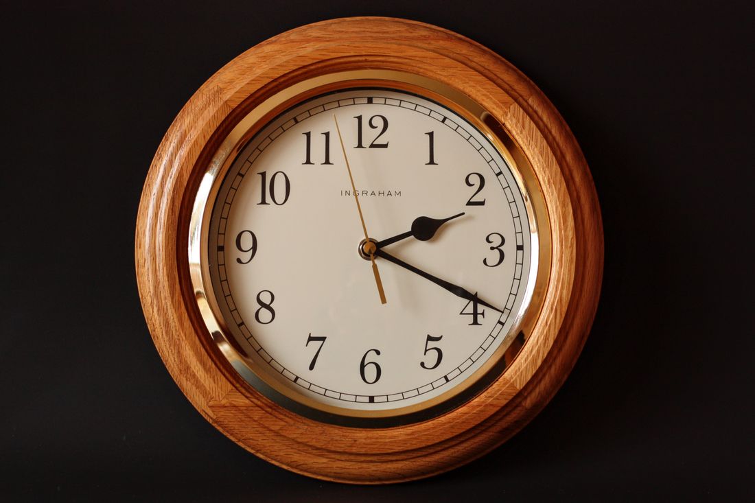 Round wooden-framed analog wall clock against a dark wall, showing time just past two o'clock