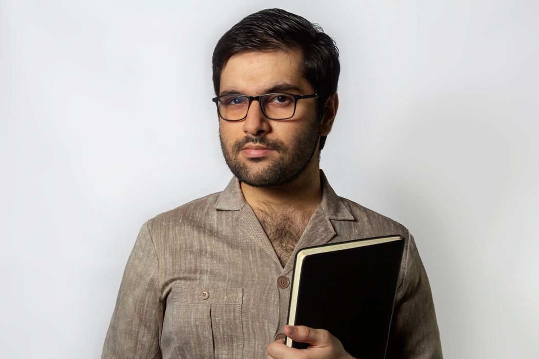 Portrait of a man in business attire with a neutral background and warm expression, holding a notebook.