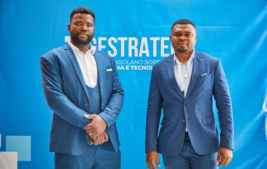 Two attendees posed for a photo in front of a large branded step-and-repeat backdrop at a conference.