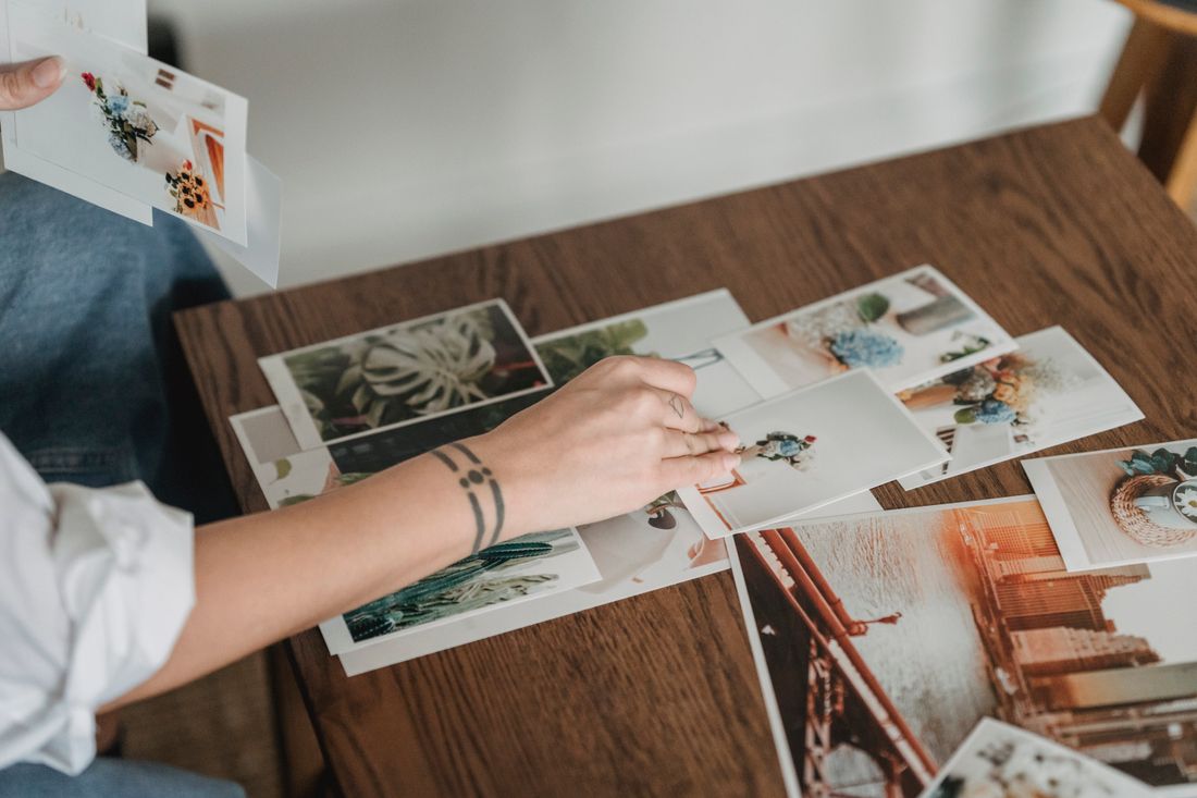 Hands arranging a spread of printed photographs across a wooden table