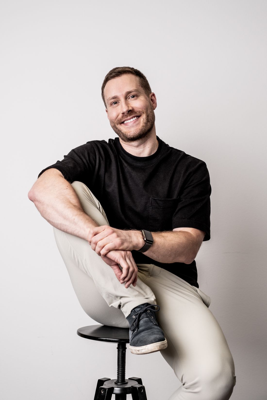 A man in a black t-shirt smiling for a studio portrait against a plain light background.