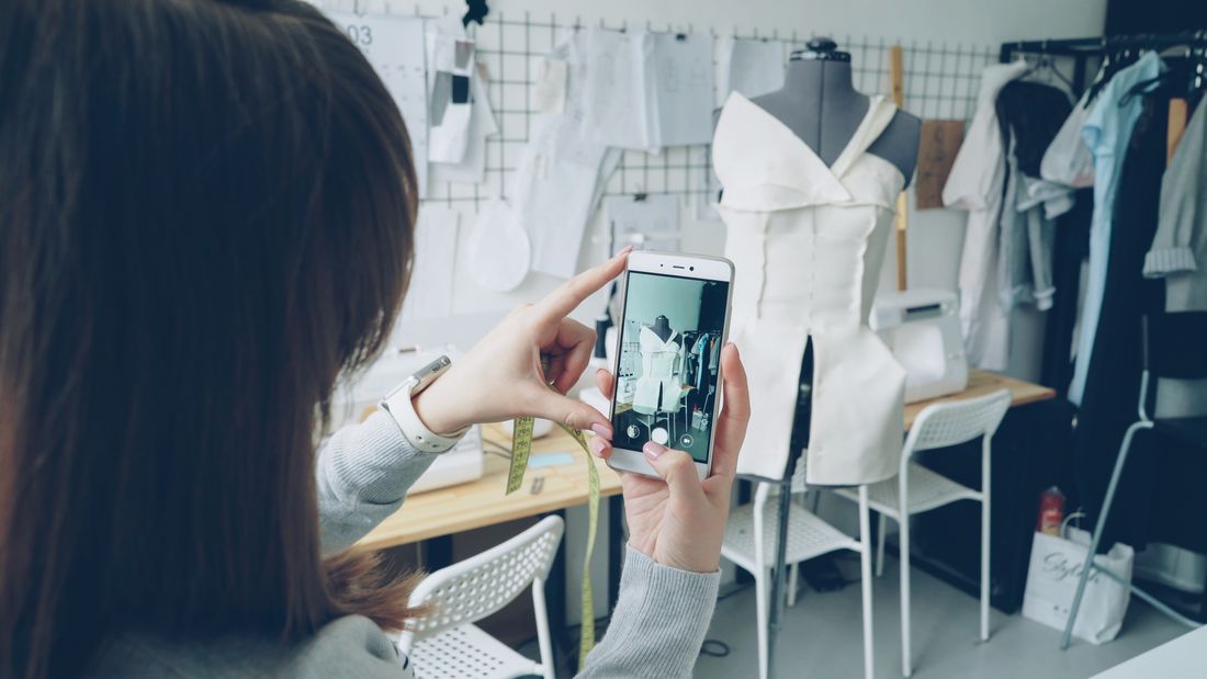 A person photographing an unfinished garment on a mannequin with a smartphone in a design studio