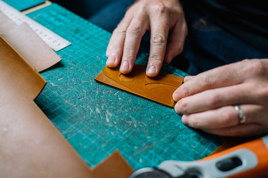 Close-up of hands working a piece of leather with cutting tools on a work mat, mid-process