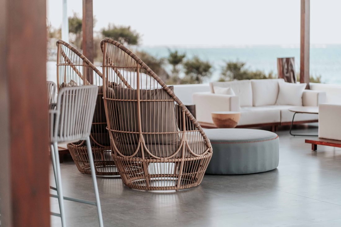 An empty outdoor terrace lounge with wicker furniture arranged for guests, staged before an amenity reveal.