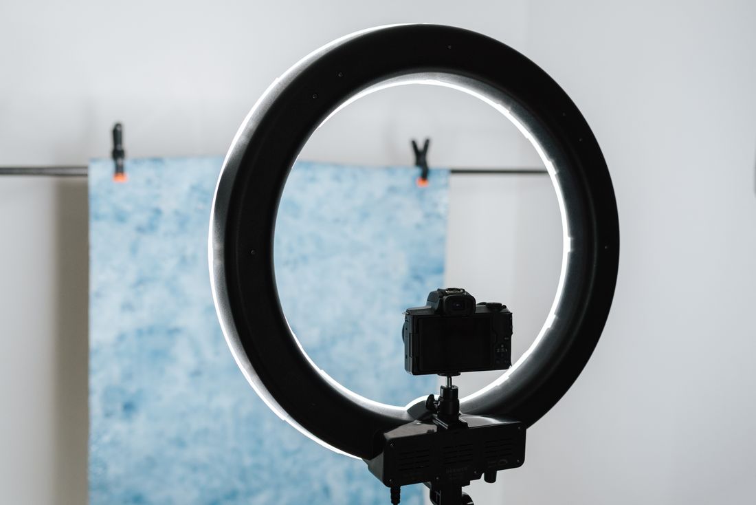 A camera on a tripod facing a small backdrop clipped to a rail, lit by a ring light in a plain room.