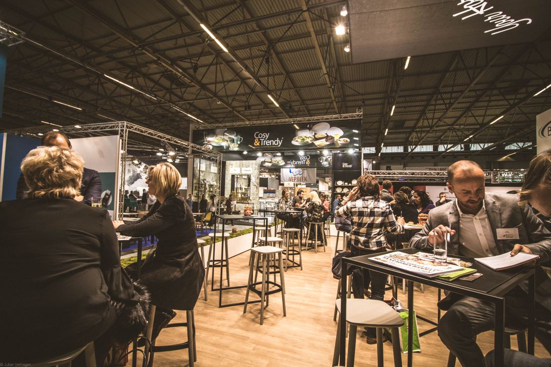 Bustling indoor trade show exhibition hall with booths and attendees at tables