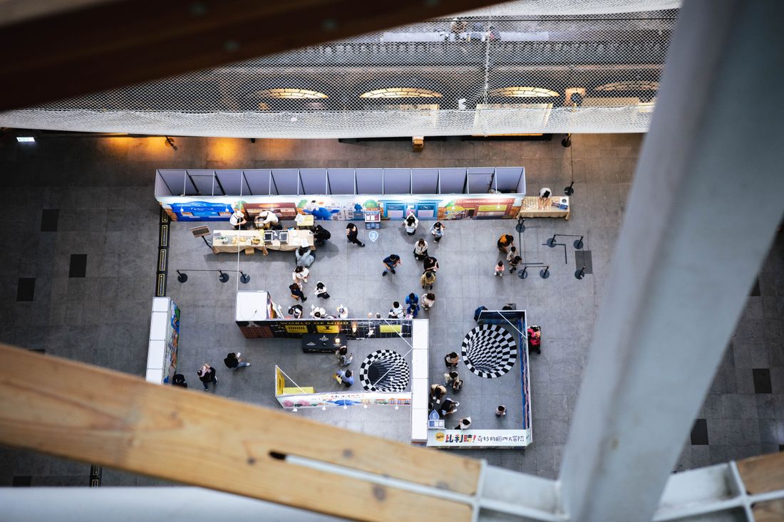 Aerial view of a busy trade show exhibition floor with rows of branded booths and attendees walking between them.