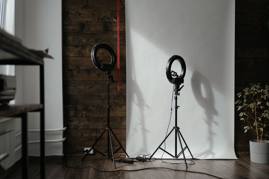 A portable photo backdrop and two ring-light stands set up against a plain wall, ready for a portrait session.