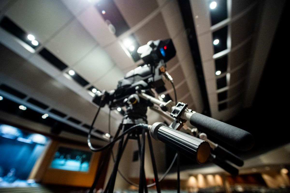 A professional video camera on a tripod in an event space with stage lighting, representing the setup used to capture clean trade show interview and demo footage