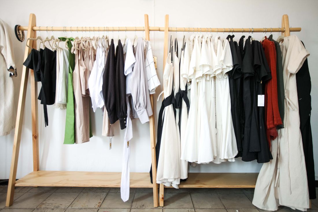 A curated selection of clothing displayed on wooden racks in a quiet showroom setting.