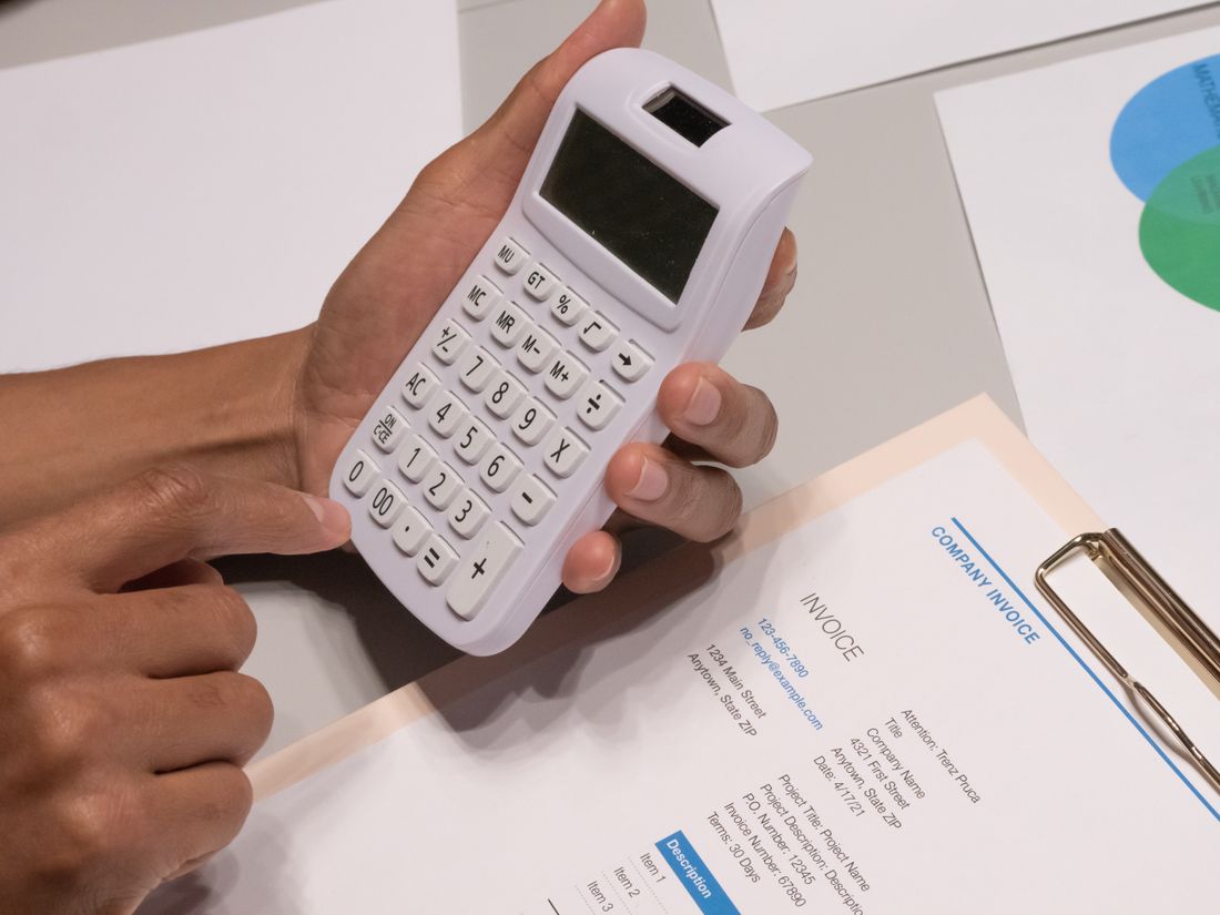 Close-up of hands holding a calculator over a printed invoice document on a desk