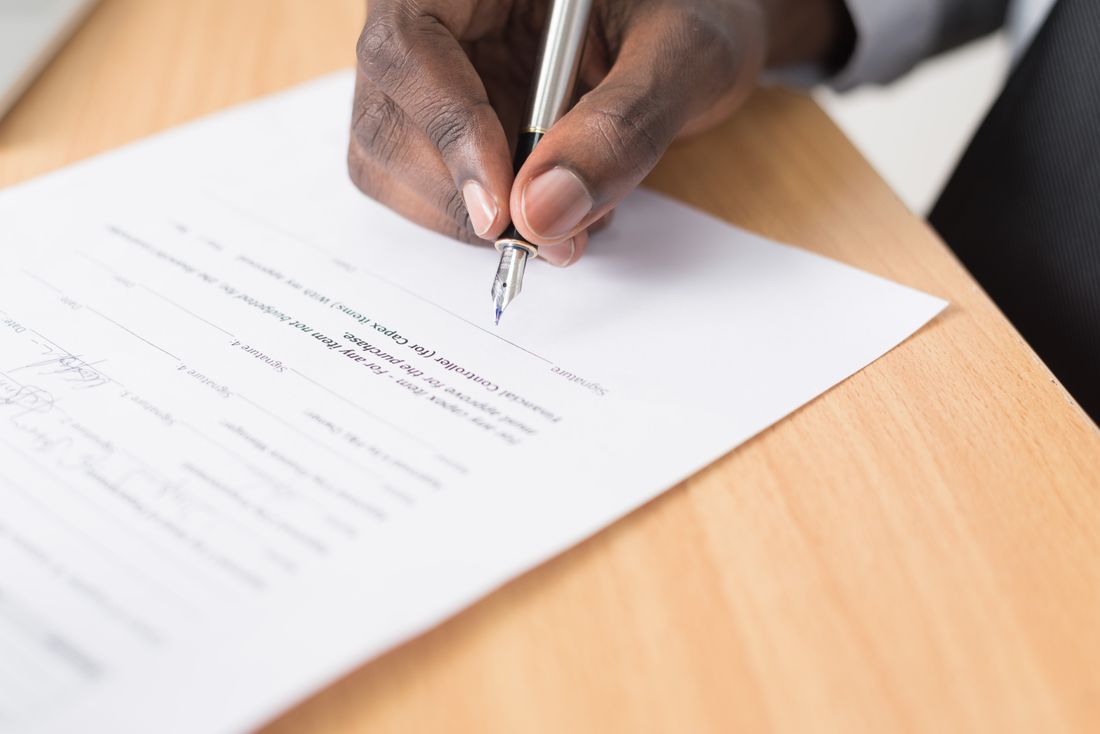 Close-up of a hand signing a printed document with a silver fountain pen on a desk