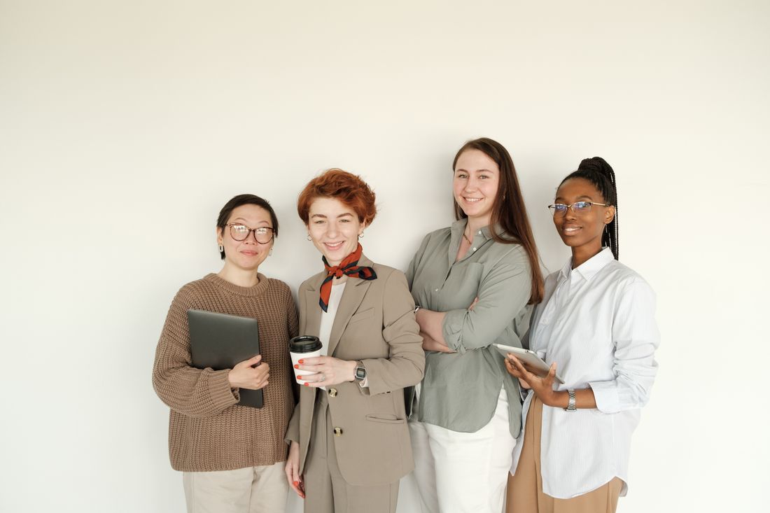 Four professionals in business-casual clothing standing together against a plain light wall, facing the camera.