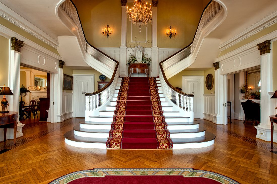 Grand double staircase with a red patterned runner in an empty historic interior, chandelier above