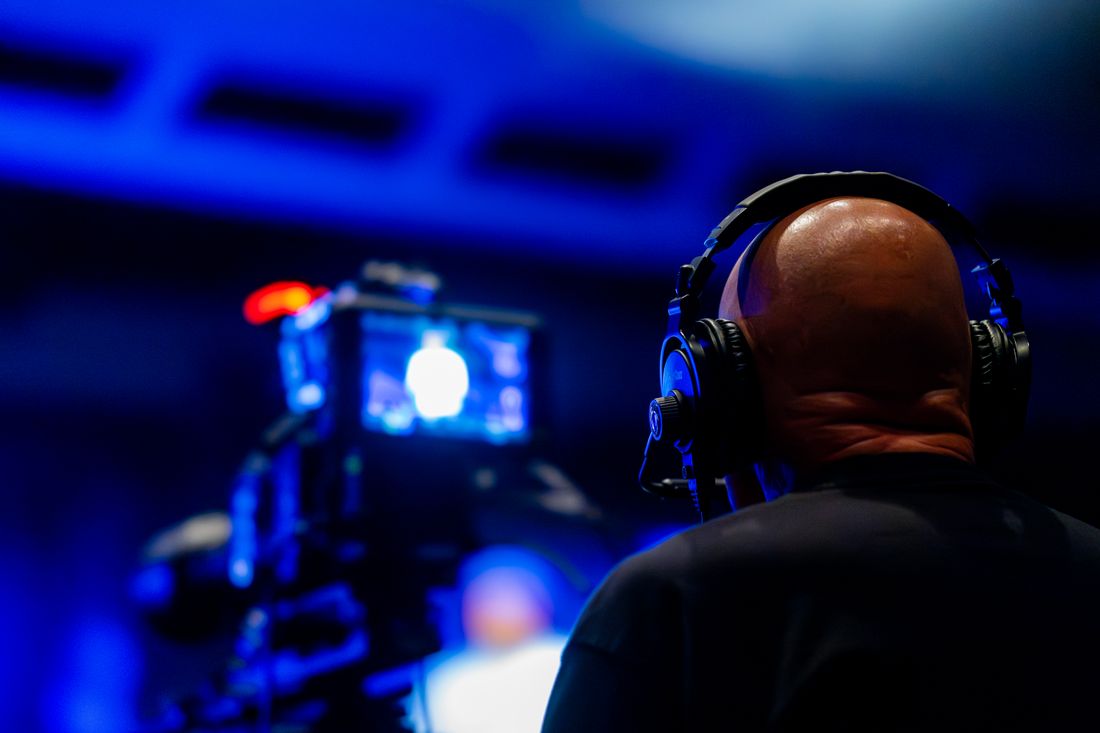 A videographer wearing headphones filming an event with professional camera equipment under blue stage lighting