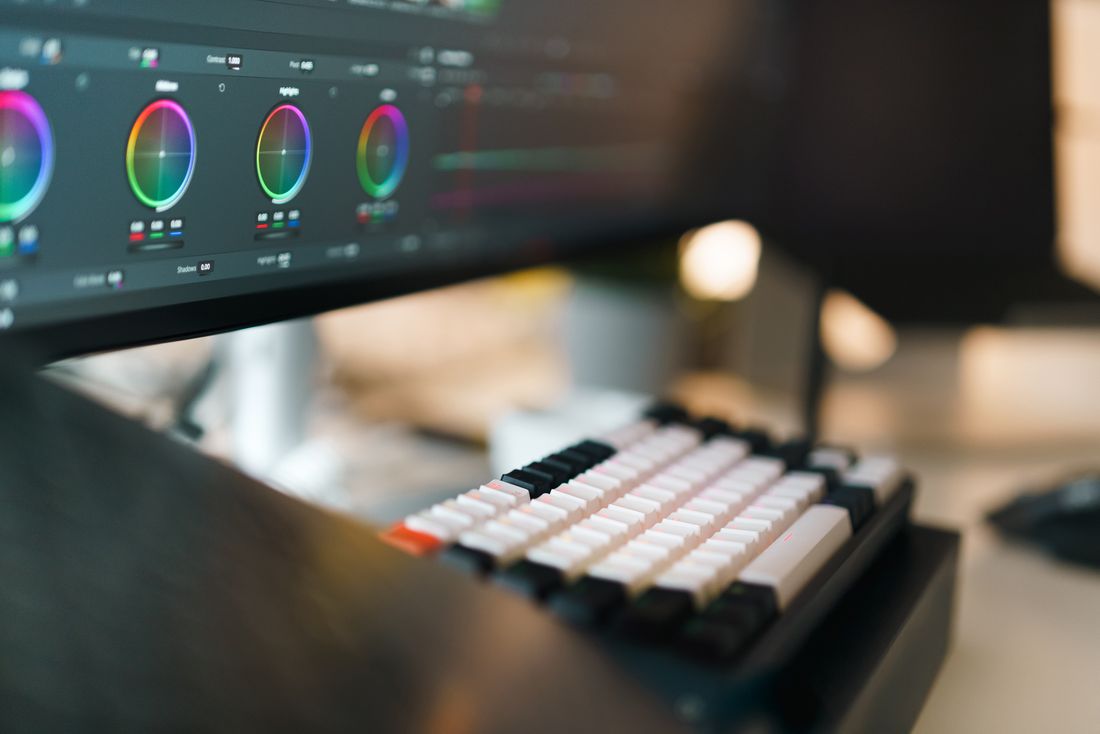Close-up of a video editing workspace with a color-grading interface on a monitor and a mechanical keyboard in the foreground
