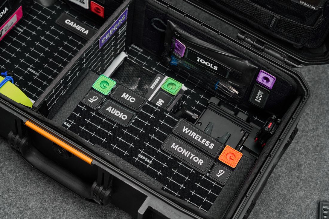 An open equipment case with labeled compartments for camera, microphone, audio, and wireless gear.