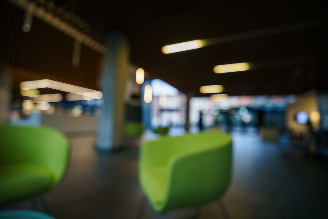 A blurred, softly lit modern office lobby lounge with green chairs, empty of people.