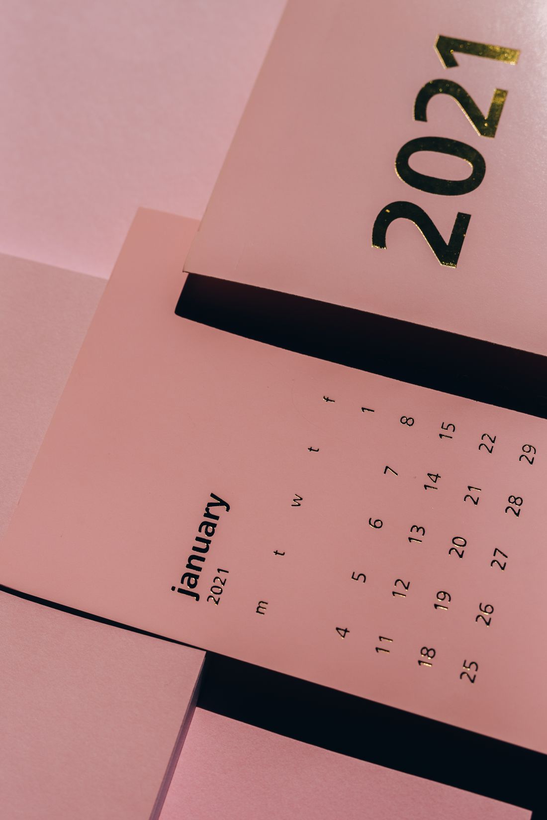 Two pink paper calendars seen at an angle on a desk, the grid of dates reading mostly as texture.