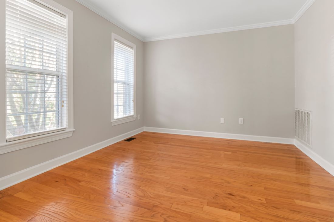 An empty room with neutral gray walls and a hardwood floor, lit by natural window light, wide and quiet before a shoot begins.