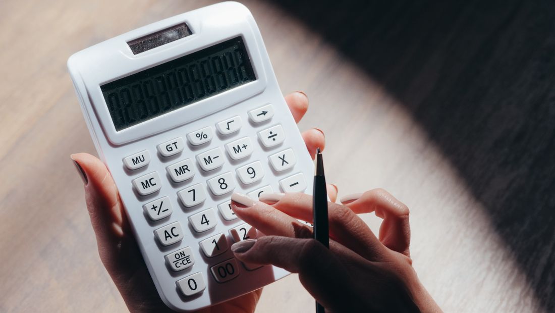 Close-up of hands holding a calculator and a pen over a notepad, working out a cost calculation.