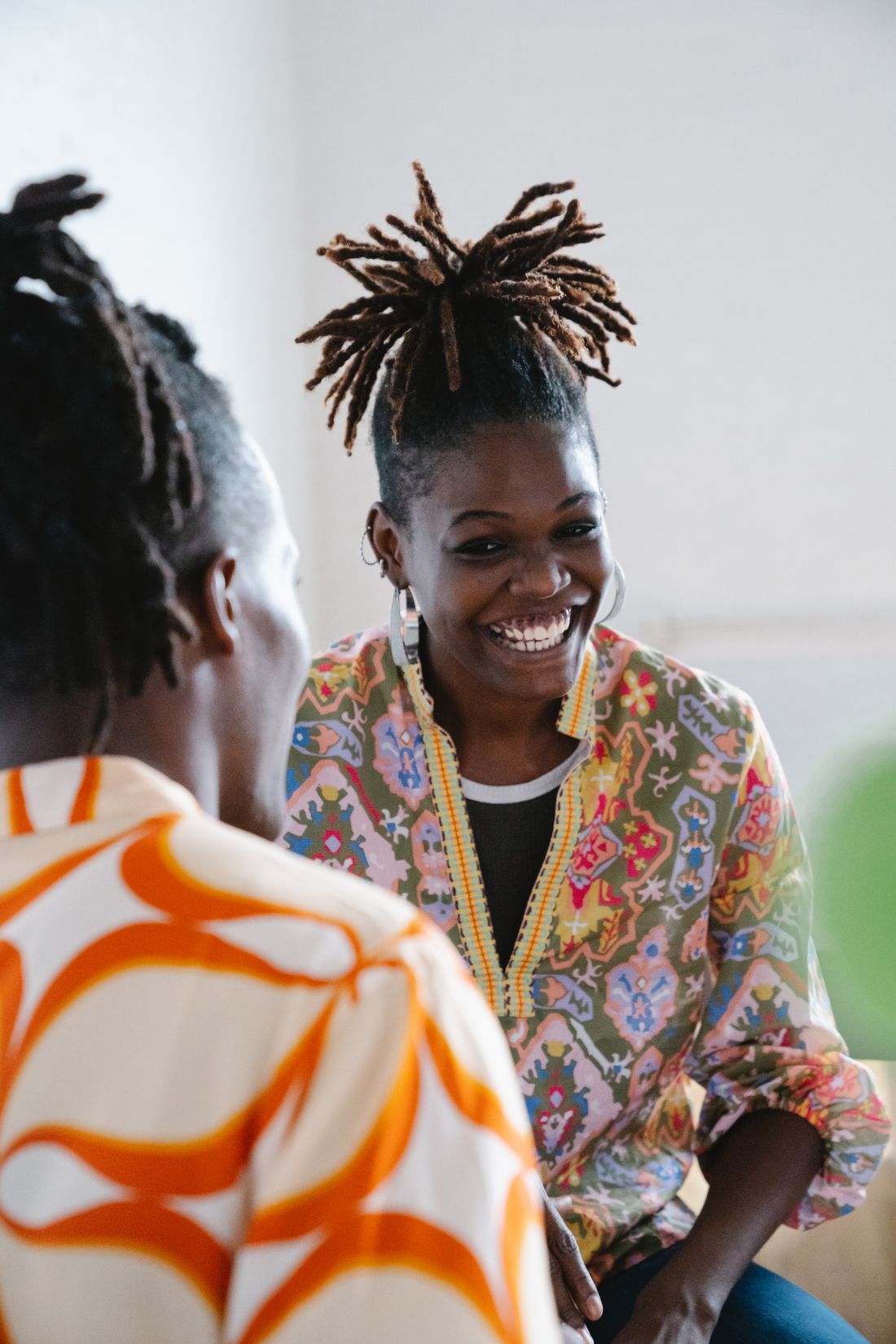 Two adults in close candid conversation indoors, one smiling warmly at the other, natural light, no equipment visible.